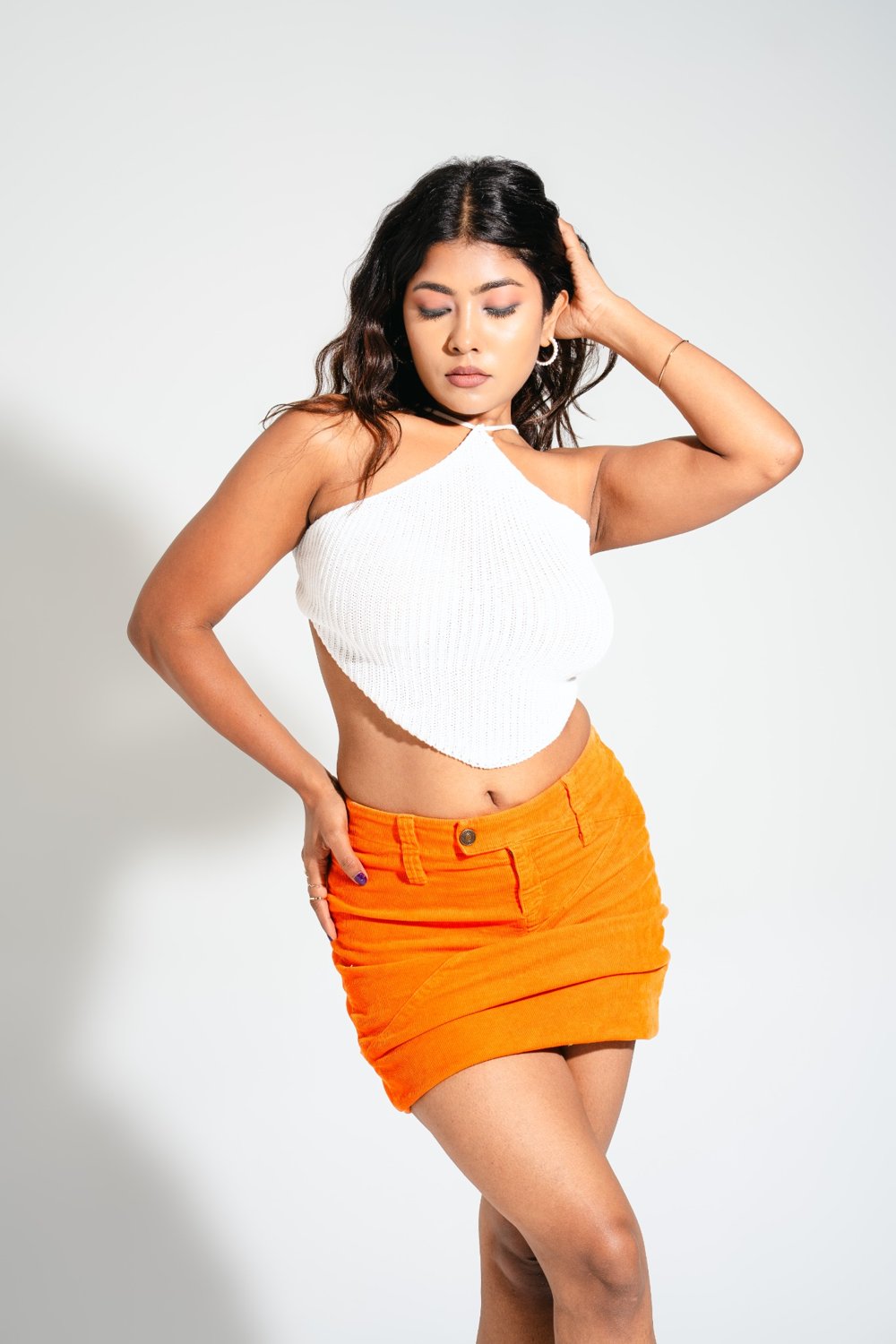 Model posing in Gia Cloud White knitted halter top paired with bright orange mini skirt — resort wear outfit