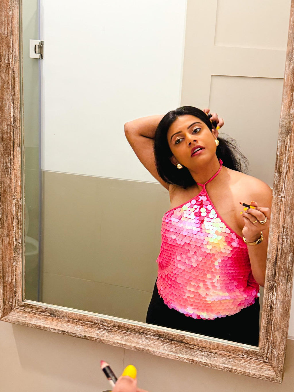 Bride-to-be wearing a pink Zoe Sequin Halter Top, applying lipstick in a mirror, styled for a Sunday glam party look with sparkly sequins and halter neckline.